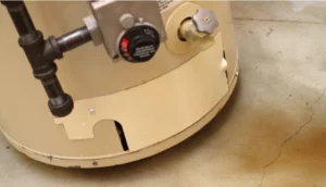 Close-up of the bottom portion of a water heater with rust-colored staining visible on the concrete floor nearby.